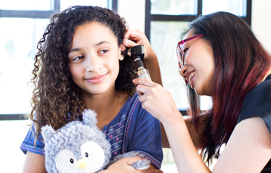 Female doctor looks in ear of tween girl holding stuffed animal