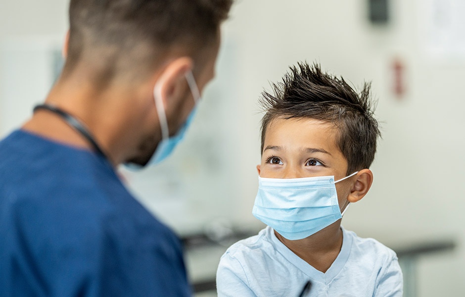 Young male patient wearing face mask listens to his doctor, a male physician also wearing face mask