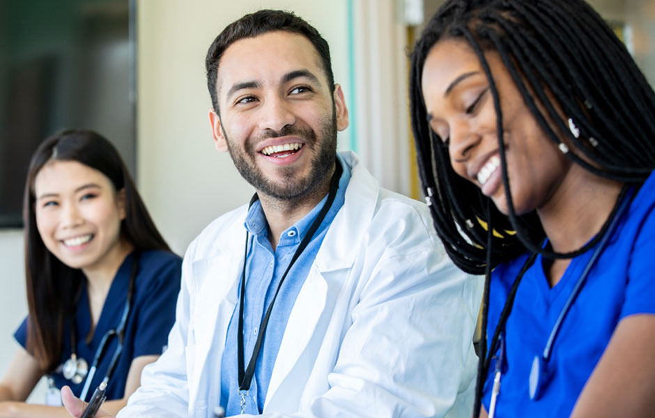 Three physicians in lab coats, scrubs and stethoscopes sit together