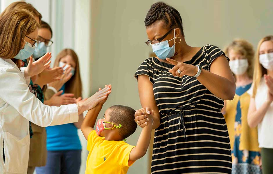 Young patient and his mom high-five as they leave a group of hospital workers, all are wearing masks.