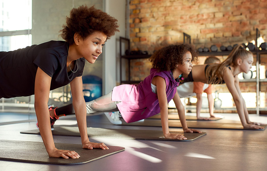 Three tween-aged kids hold a yoga pose in a studio