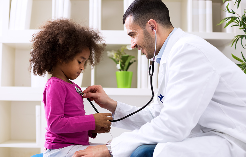 Close-up of male doctor with stethoscope listening to heart of female toddler