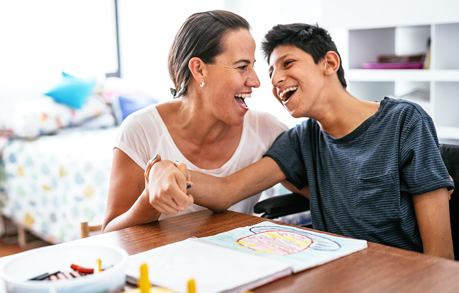 Mother and teen son smile and laugh while coloring at home