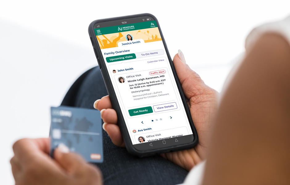 The hands of a woman holding a credit card and a cell phone displaying the Nemours app