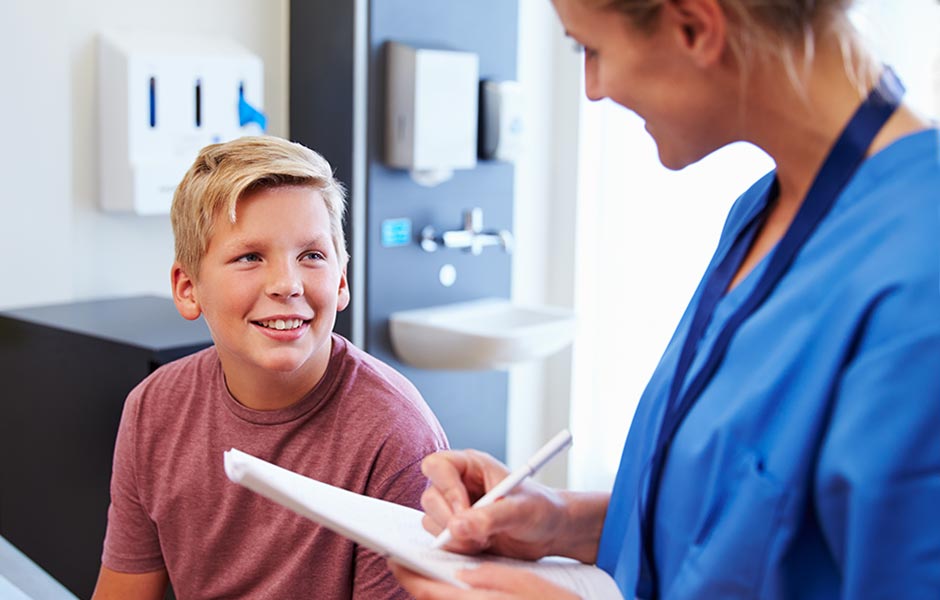 Healthcare provider in scrubs with paperwork and pen speaks with a young patient. 