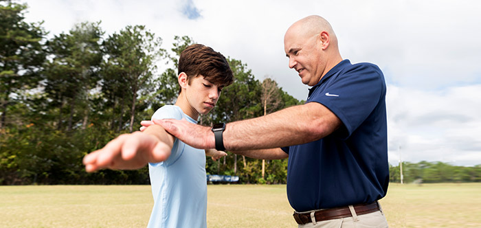 Male teen with arms extended for testing by adult male coach on sports field