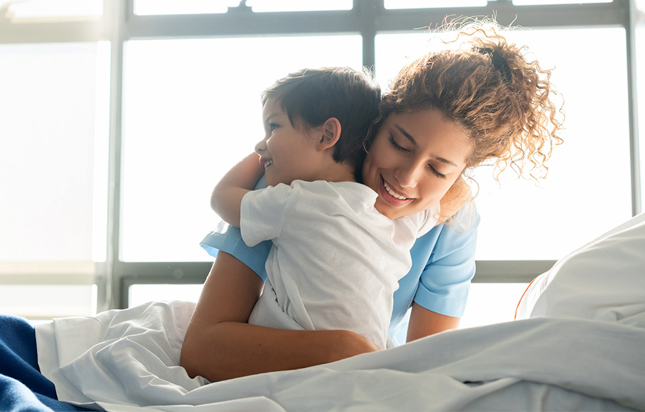 Female caregiver hugs smiling toddler in a hospital bed Woman caregiver hugs smiling toddler in a hospital bed
