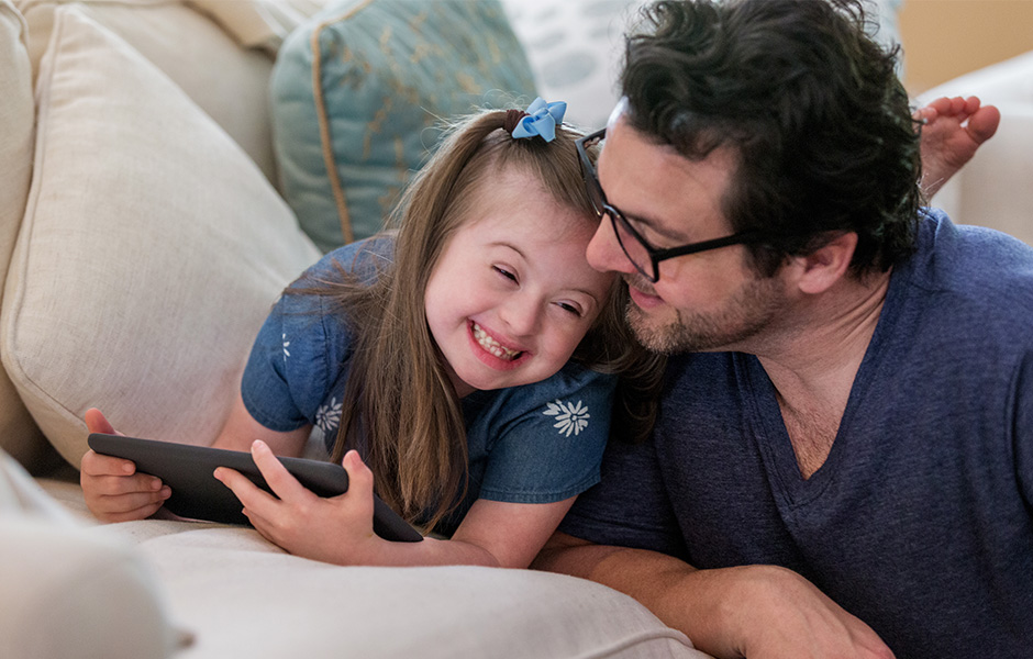 Close-up of man and school-age girl relaxing and laughing with a tablet