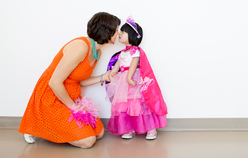 Mother kneels down to kiss her young child, who is dressed in a costume and a crown. 