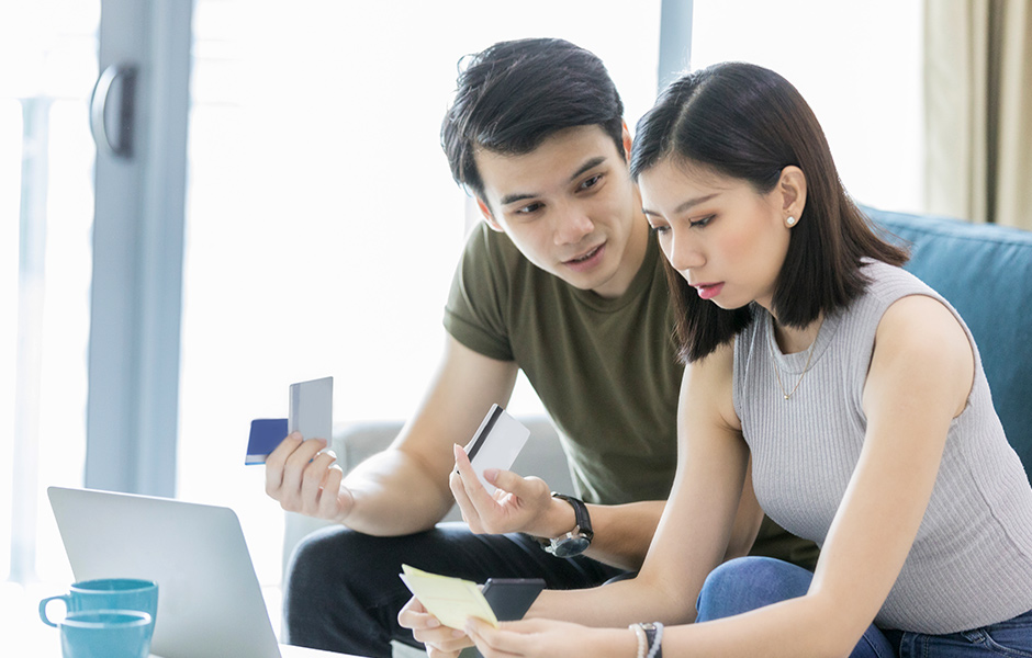 Couple hold credit cards as they pay a bill on their laptop