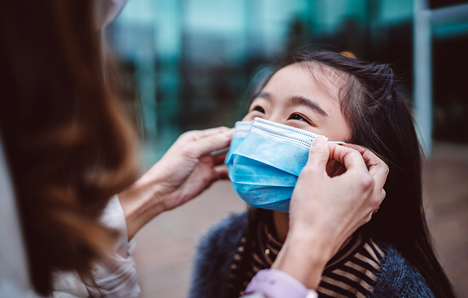 Adult placing mask on school-age girl Close-up of an adult placing a face mask on school-age girl