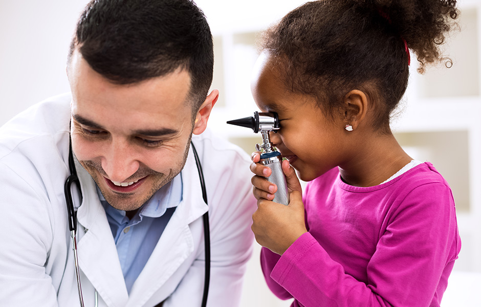 Young girl uses otoscope to look in ear of male doctor