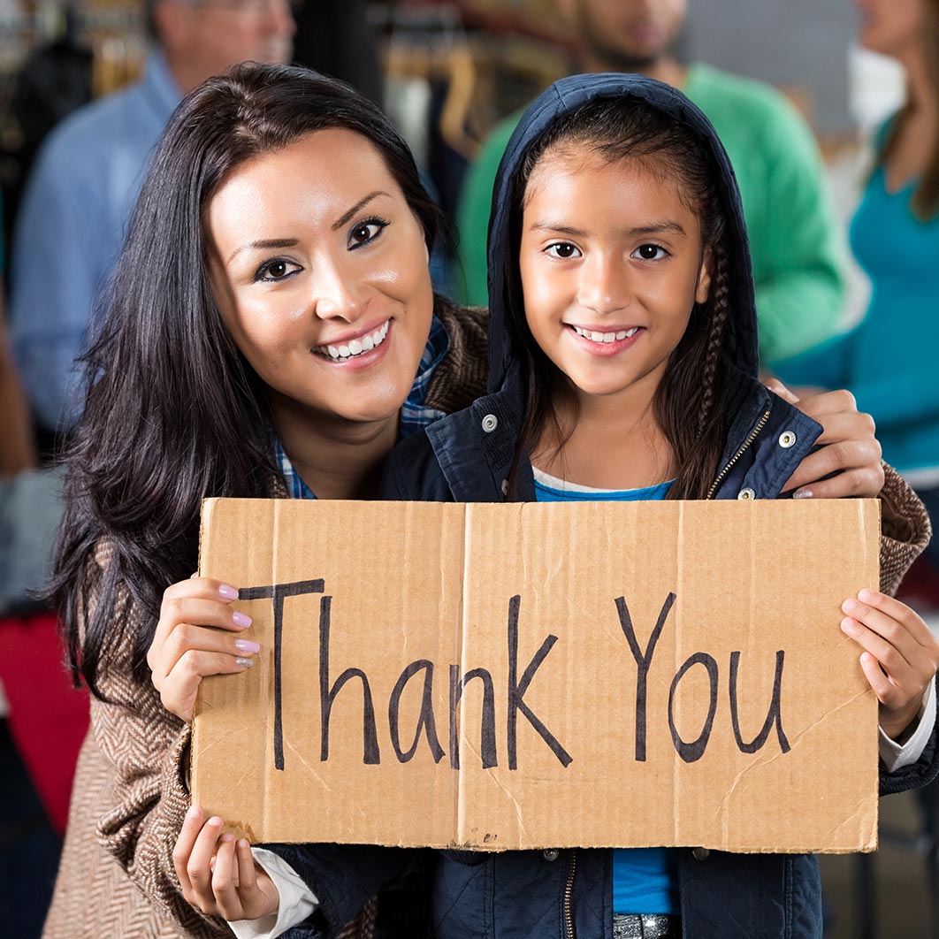 Mother and daughter stand side-by-side smiling, holding a handmade sign that reads "Thank You"
