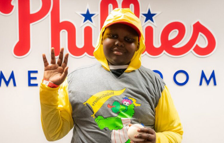 Kaden, a lymphoma patient, standing in front of a Phillies sign.