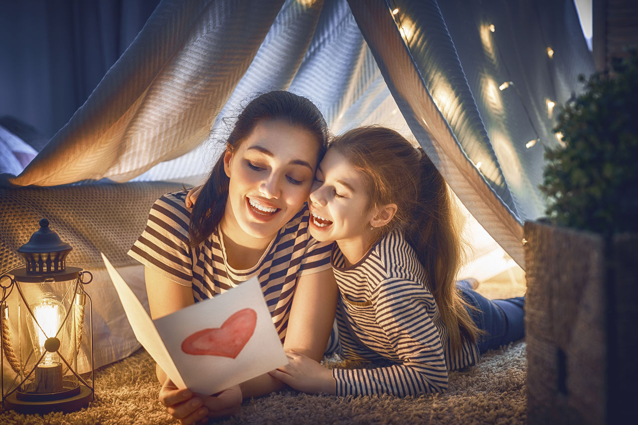 A mother and daughter laying under a tent reading together under fluorescent light.