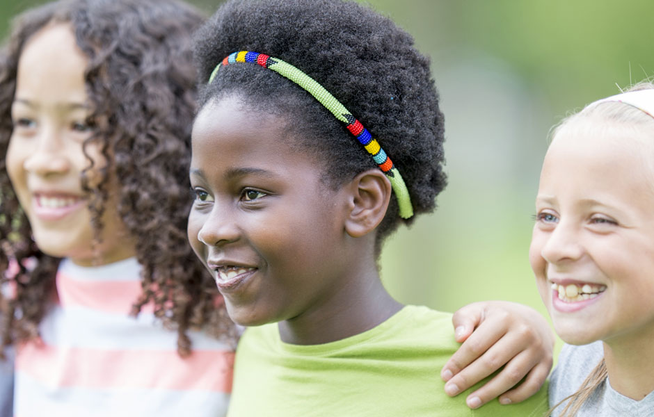 Three school-aged kids stand shoulder-to-shoulder smiling