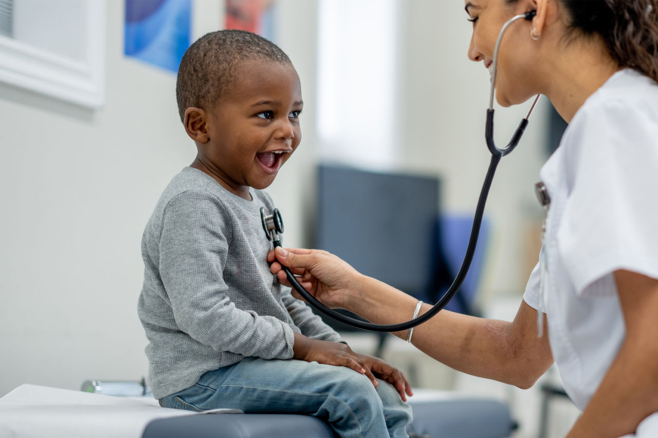 Un niño feliz con su médica que escucha su respiración.