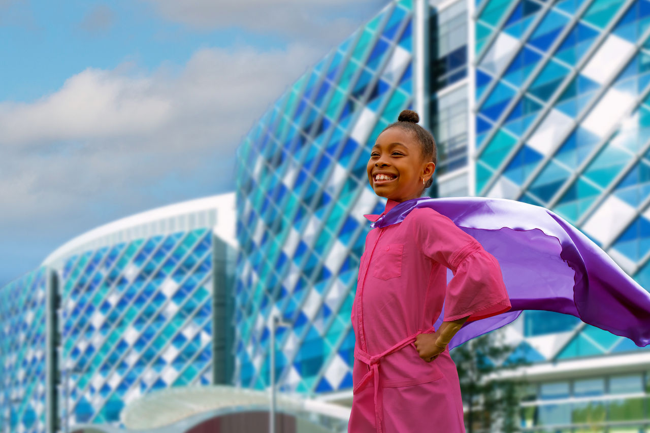 Patient posing like a superhero with a cape in front of Nemours Children's Hospital