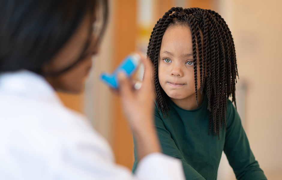 Female doctor in lab coat demonstrates asthma inhaler to a young child