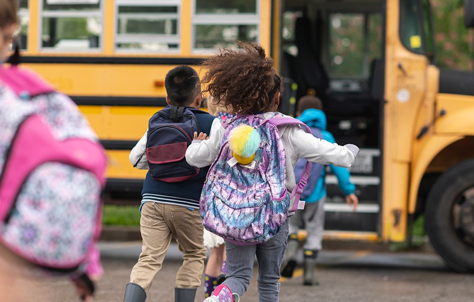 Male and female kids run to the open schoolbus door wearing backpacks