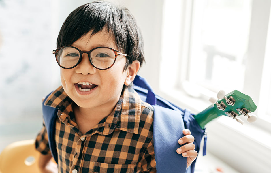 Un estudiante de primaria con mochila y guitarra que usa gafas. 