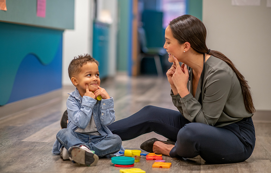 Toddler patient works with female provider using hands to make facial expressions. Toddler patient works with female provider using hands to make facial expressions.