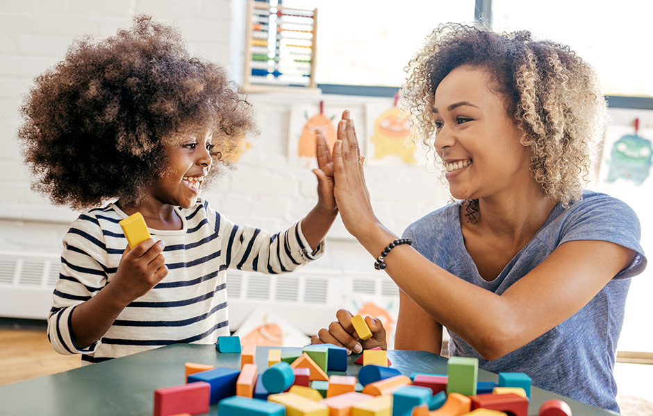 Child and provider high-fiving while working with blocks.