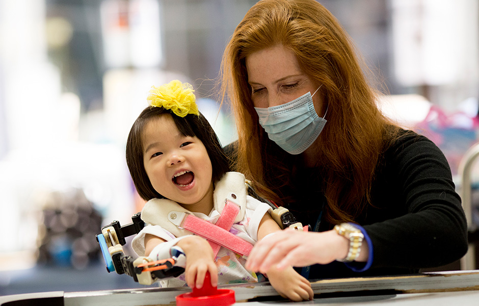 Young girl who uses assistive device, laughing and working with therapist