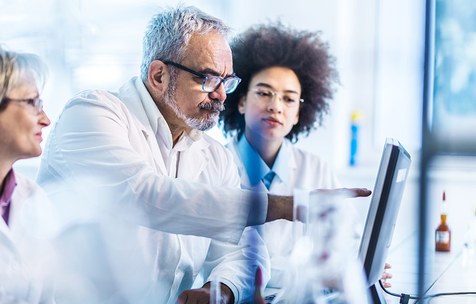 Male research doctor pointing at a computer monitor, with doctors beside him