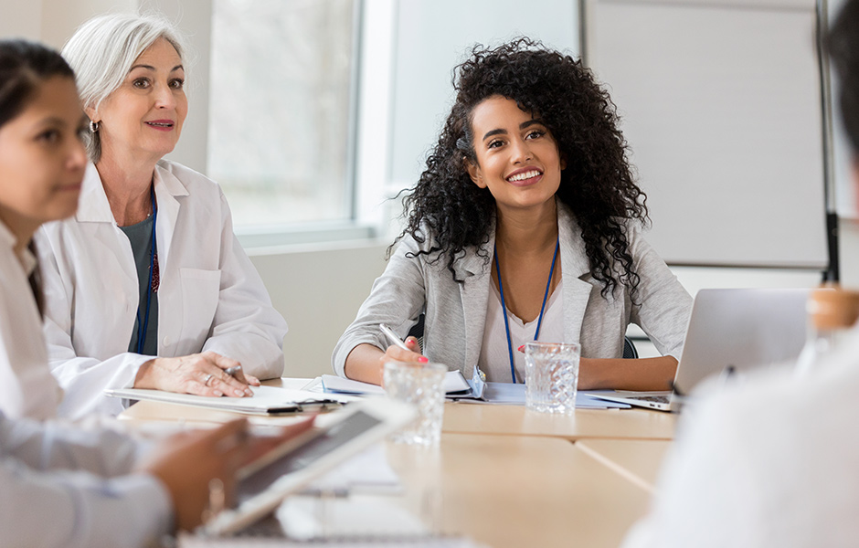 Female doctors in lab coats seated around conference table