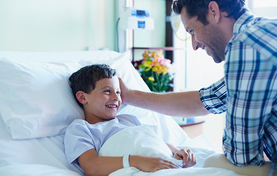 Father comforting son in hospital bed.