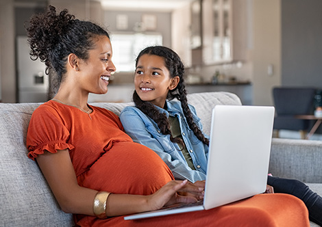 Young mom and her daughter sit on couch with a laptop at home 