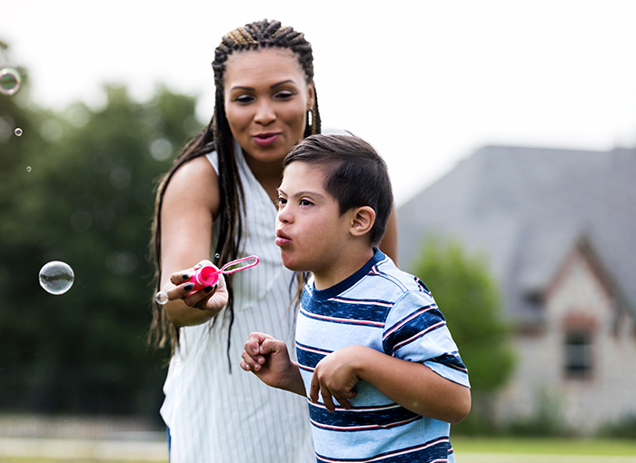 School-aged boy with special needs outside blowing bubbles with help of his caregiver. 