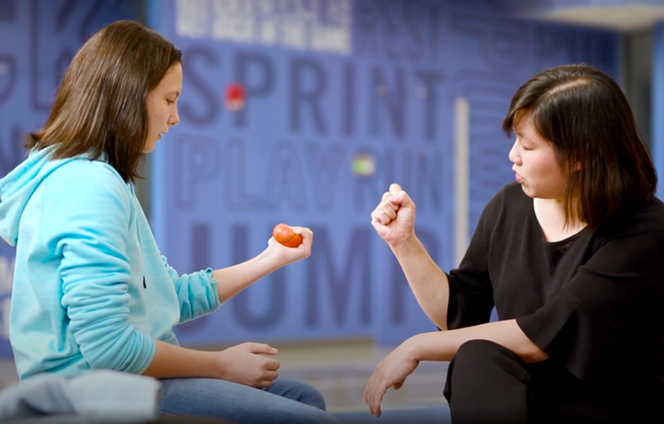 Teenage female patient squeezes a hand therapy ball as instructed by female hand therapist.