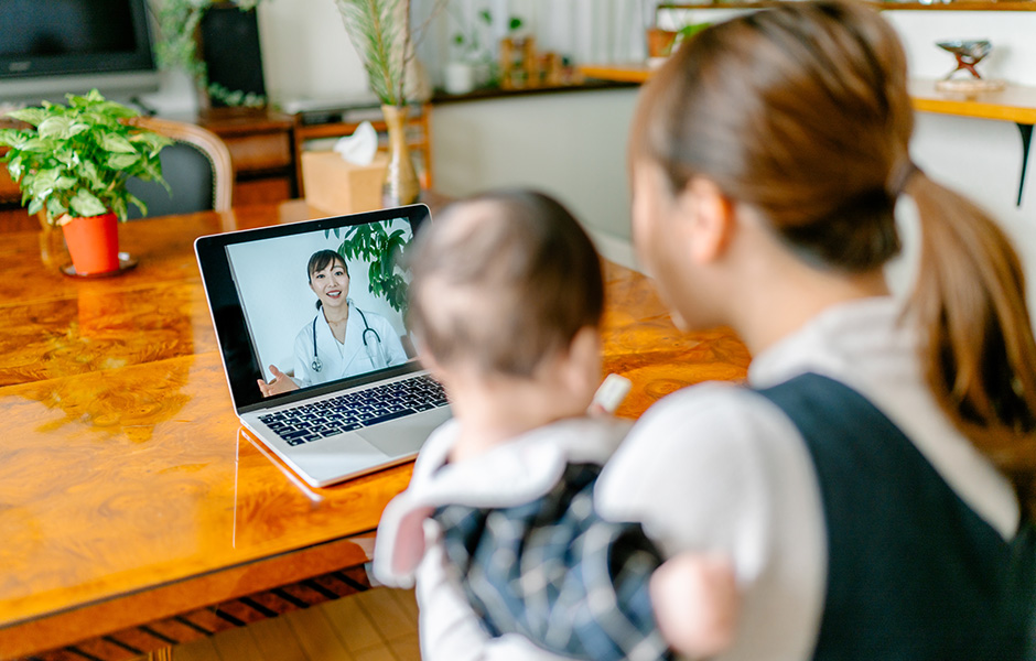 Una madre que sostiene a su bebé mientras mira al médico a través de una computadora portátil durante una visita de telesalud