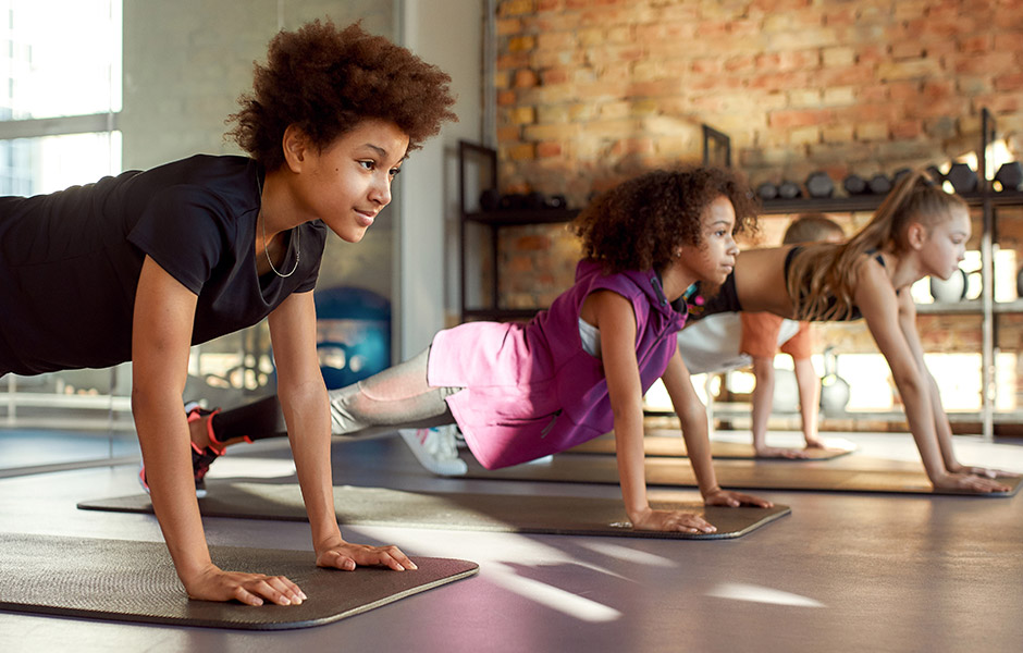 Three tween-aged kids hold a yoga pose in a studio Three tween-aged kids hold a yoga pose in a studio