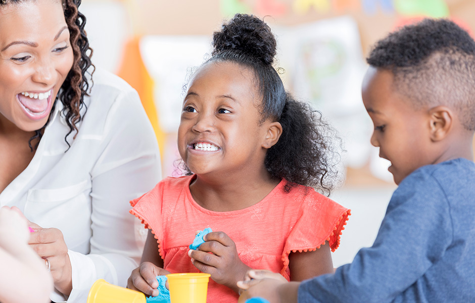 Adult female laughing with her two children at a play table, one is special needs