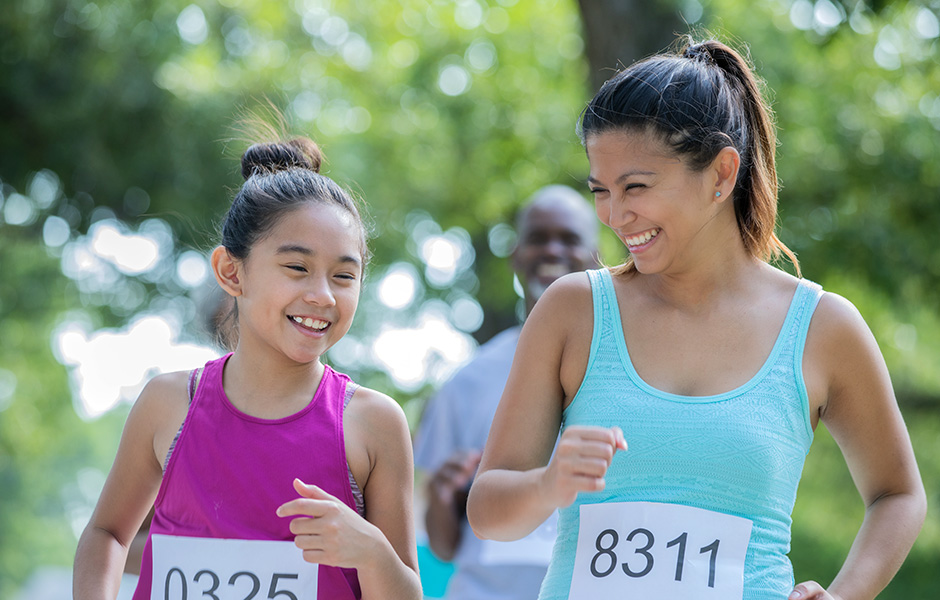 Girl and woman 5k style wearing tanktops and runner numbers Girl and woman smiling and running in group, wearing tanktops and runner numbers