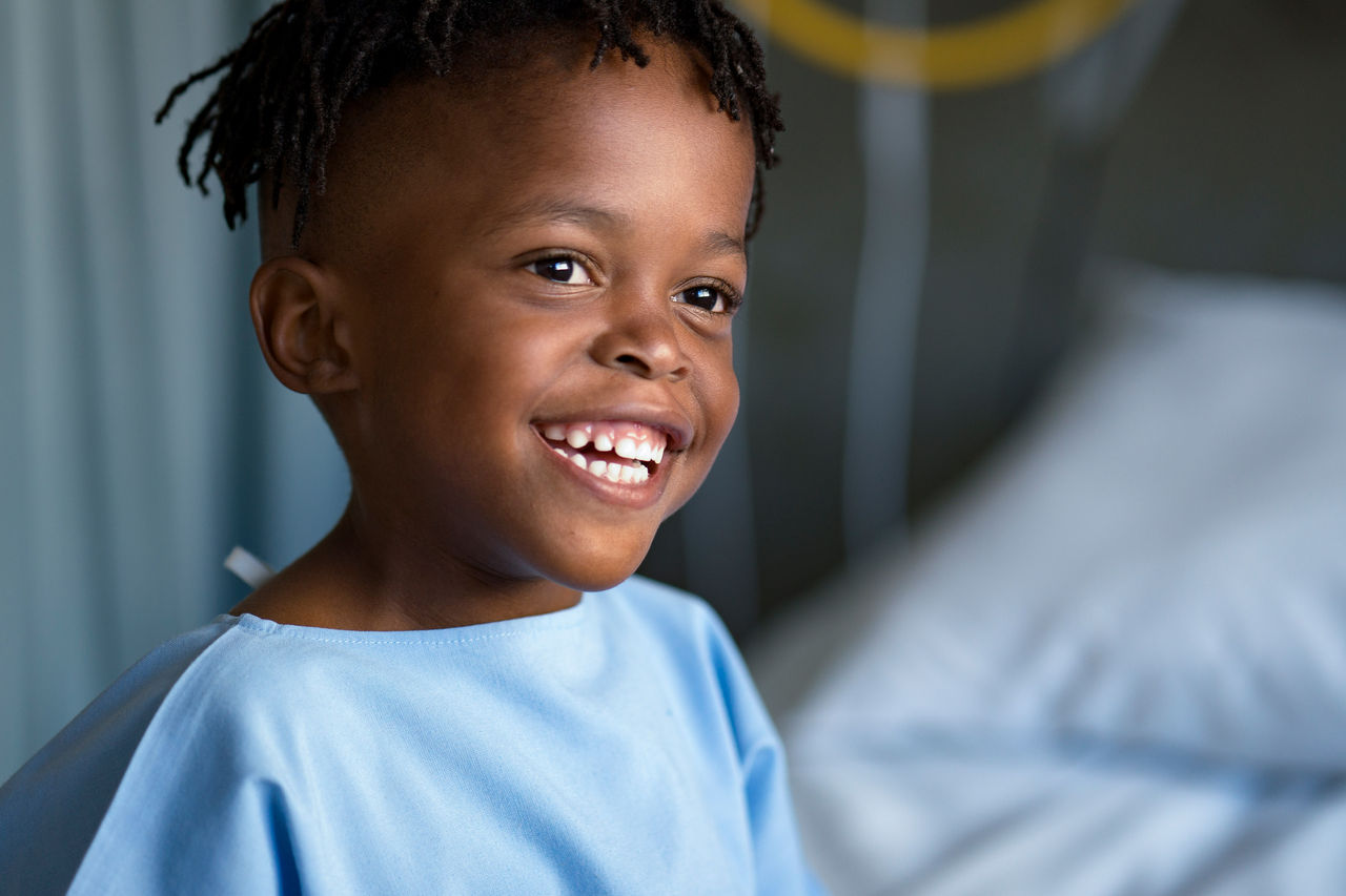 Young boy wearing a hospital gown smiling while sitting on a hospital bed