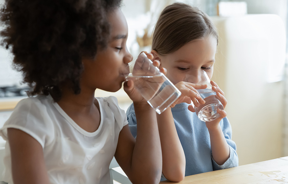 Two young girls sit at a kitchen table drinking water