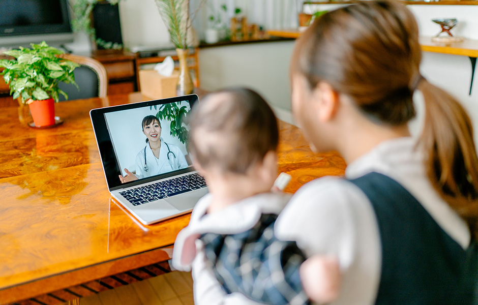 Mother holding infant looking at doctor on laptop during a telehealth visit