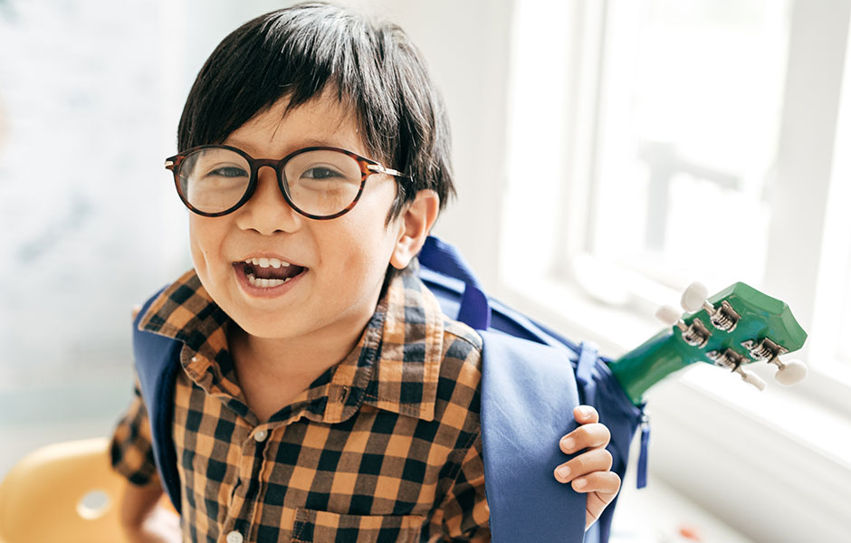 Elementary student with backpack and guitar wearing glasses. 