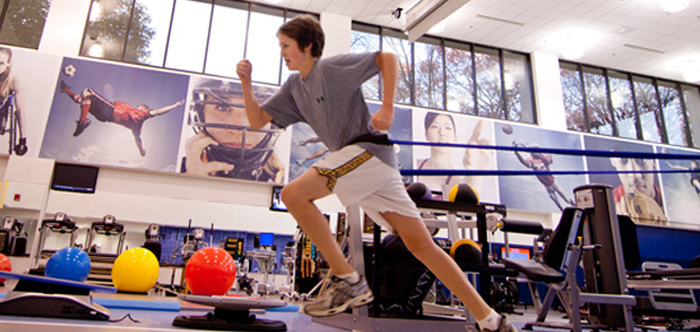 Male teen doing physical therapy with band around waste in gym