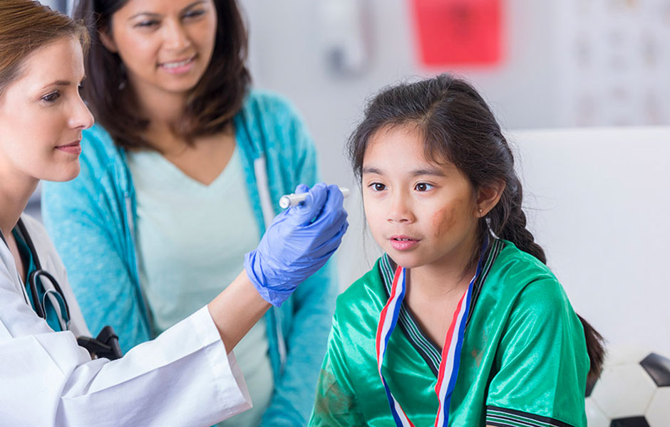 Young female soccer player wears a medal around her neck while female doctor examines her and mom stands next to them