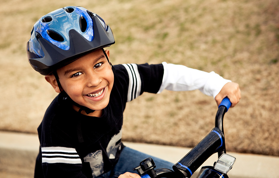 Young smiling boy on a bicycle wearing a safety helmet. 