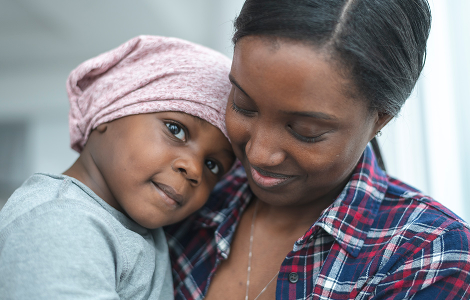 Young mom holds toddler daughter who wears a pink head scarf.