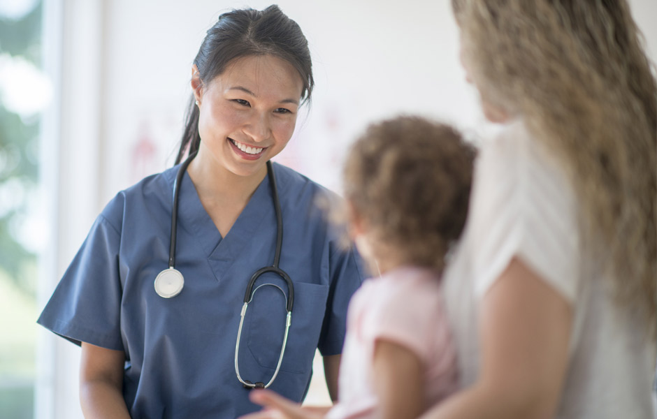 Una médica que les sonríe a una niña pequeña y a su madre. 