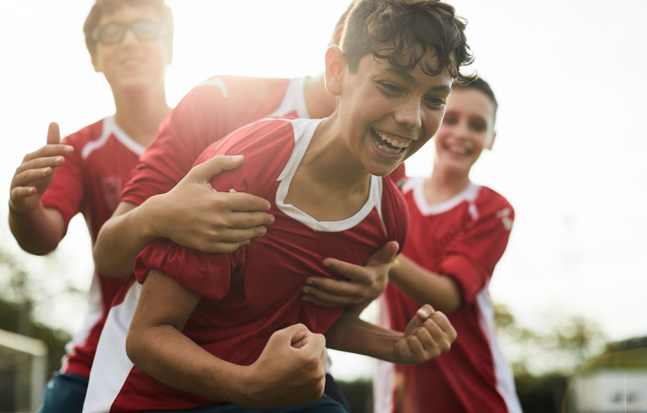 Teenage boys in soccer uniforms are sweaty post-game and they are laughing and celebrating